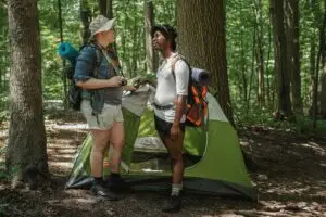 Diverse couple setting up camp in a forest during a summer hike, showcasing adventure and inclusivity.