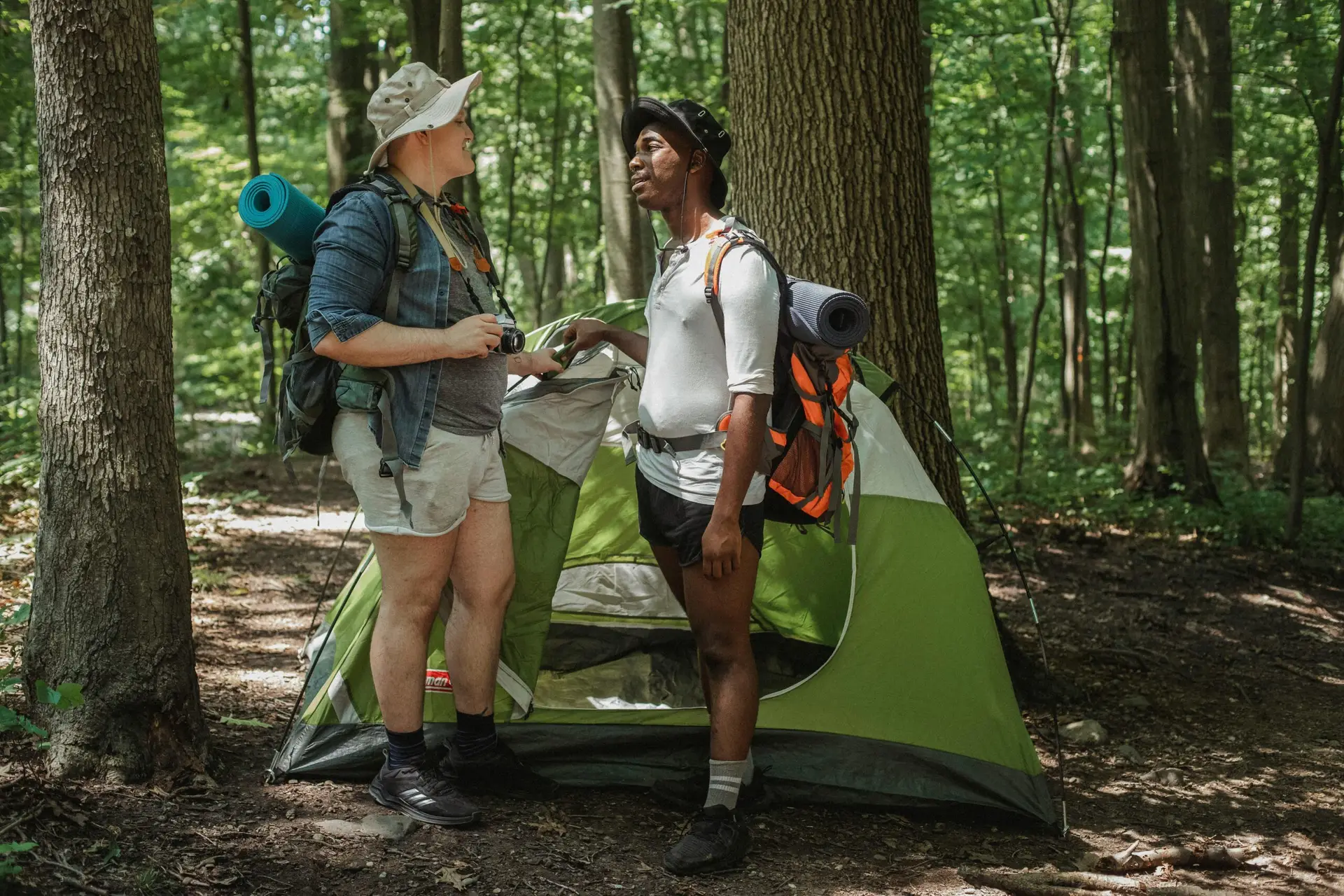 Diverse couple setting up camp in a forest during a summer hike, showcasing adventure and inclusivity.