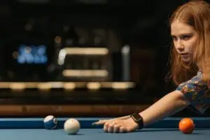 Young woman playing billiards indoors, focusing on her next shot under dim lights.